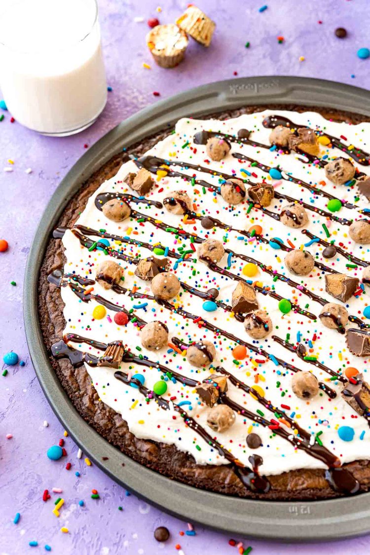 Close up photo of brownie dessert pizza in a pan on a purple surface with candy scattered around.