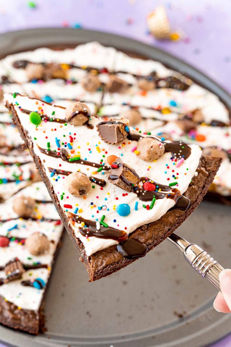 Slice of brownie pizza being lifted away from the whole pizza on a serving spatula.