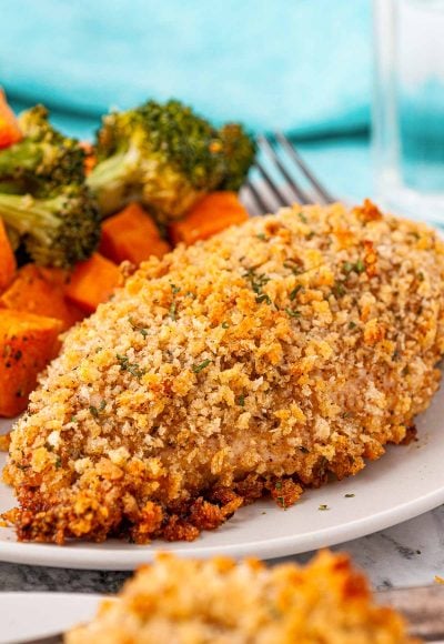 Breaded chicken breast on a white plate served with vegetables.