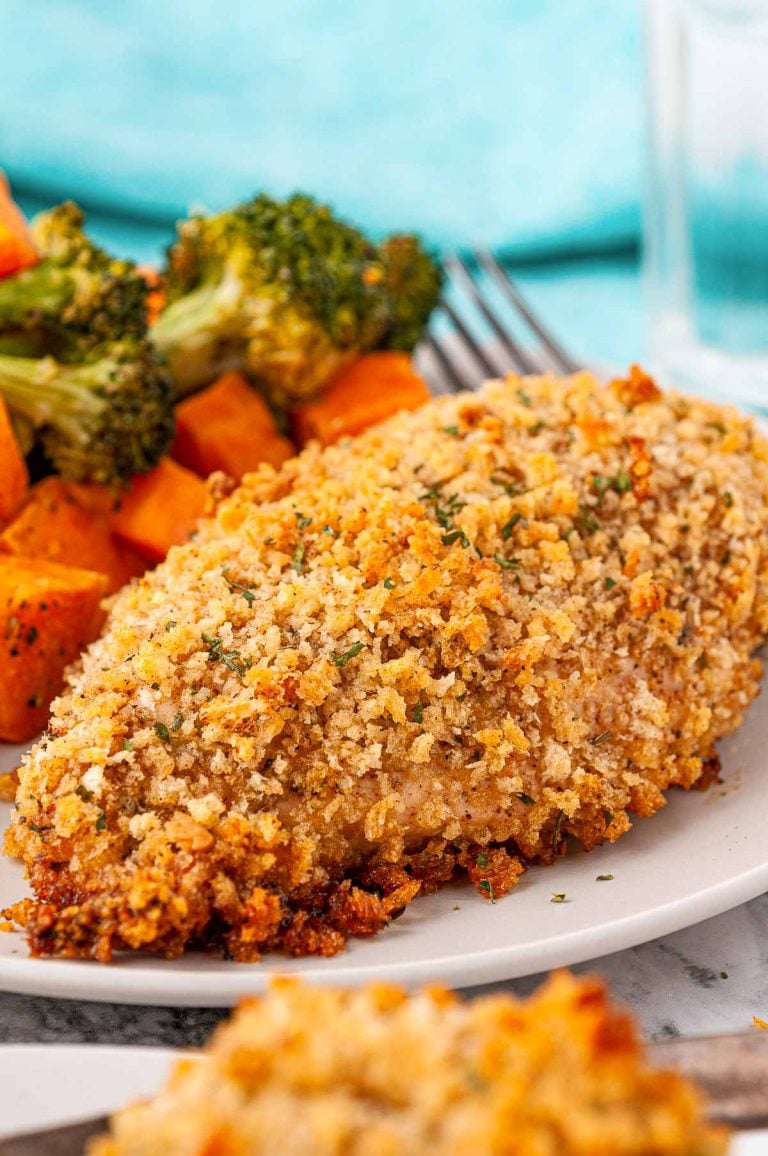Breaded chicken breast on a white plate served with vegetables.