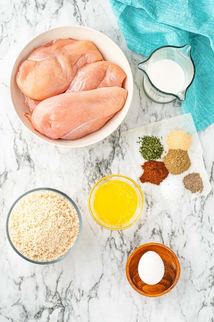 Ingredients to make breaded baked chicken on a marble table.