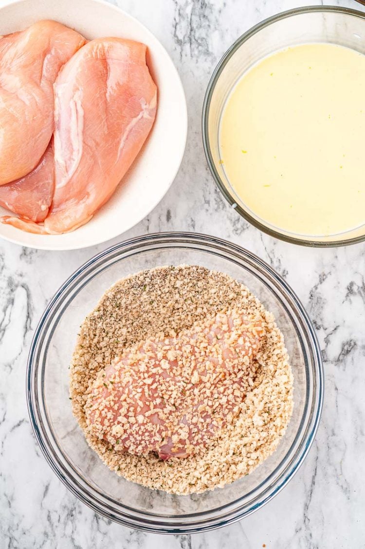 Chicken being breaded in prep bowls.