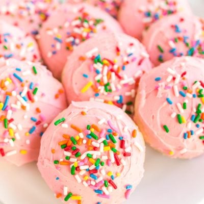Close up photo of pink frosted sugar cookies on a plate covered in sprinkles.