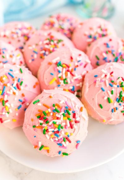 Close up photo of pink frosted sugar cookies on a plate covered in sprinkles.