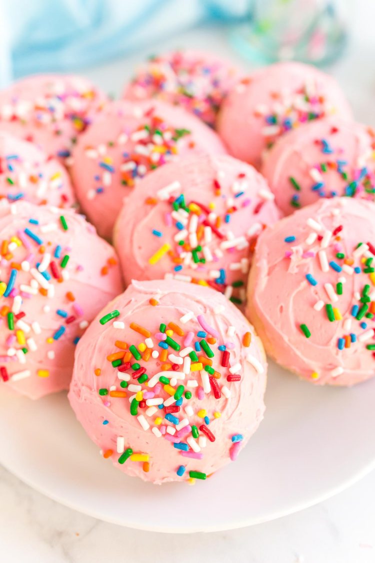 Close up photo of pink frosted sugar cookies on a plate covered in sprinkles.