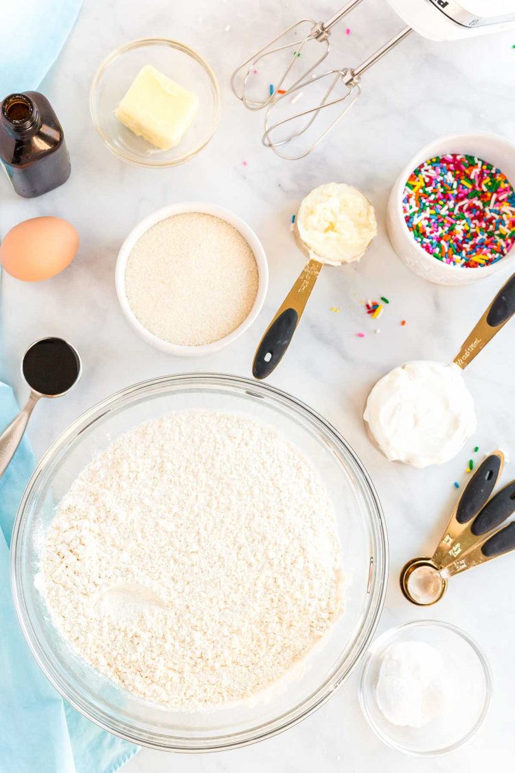 Ingredients to make sugar cookies on a white marble countertop.