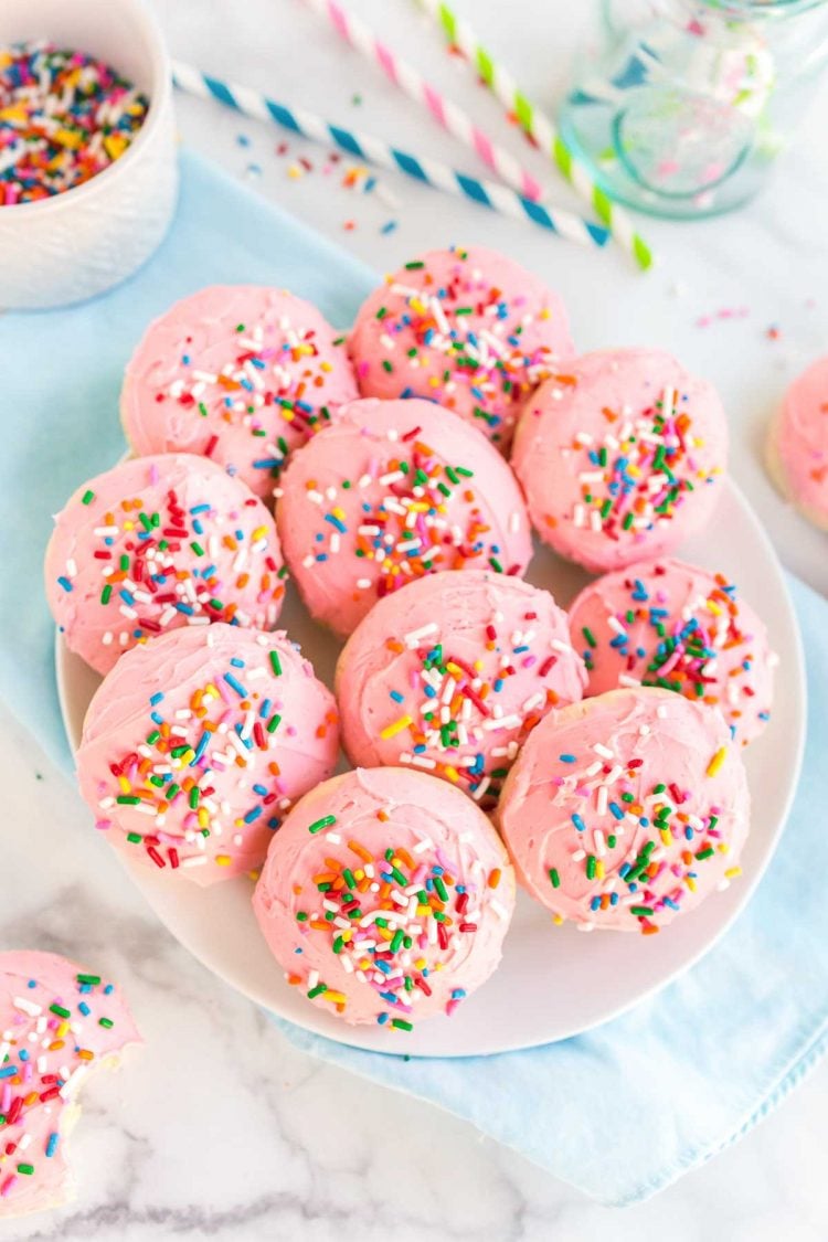 Pink frosted sugar cookies on a white plate on top of a blue napkin.