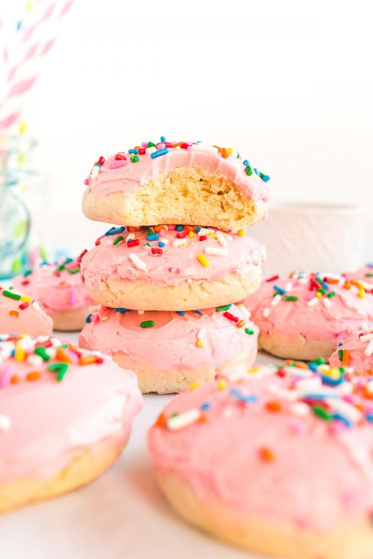 Pink frosted sugar cookies stacked on top of each other, the top one has a bite taken out of it.