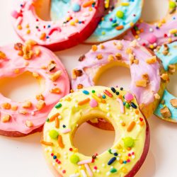 Apple donut slices topped with cream cheese frosting and sprinkles on a white plate.