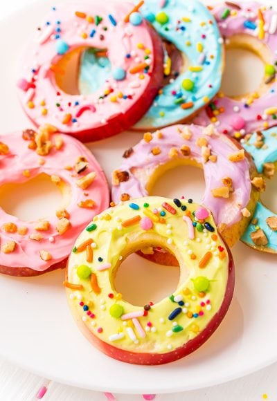 Apple donut slices topped with cream cheese frosting and sprinkles on a white plate.