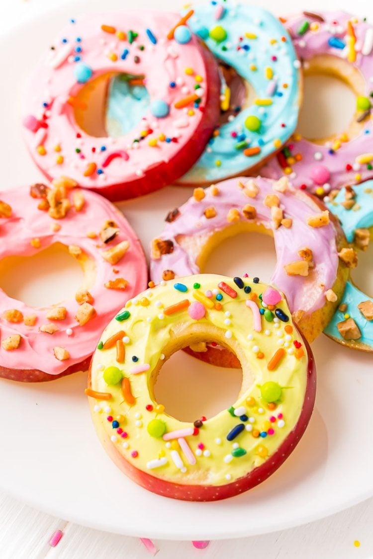 Apple donut slices topped with cream cheese frosting and sprinkles on a white plate.