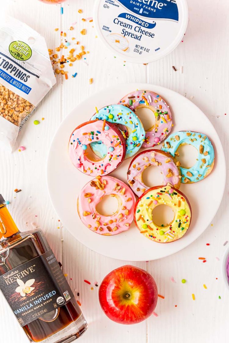 Apple donut slices on a white plate with the ingredients to make them scattered around.