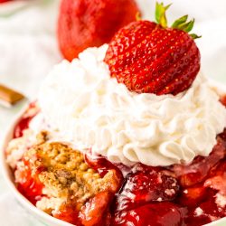 Strawberry dump cake on a white plate topped with whipped cream and a fresh strawberry.