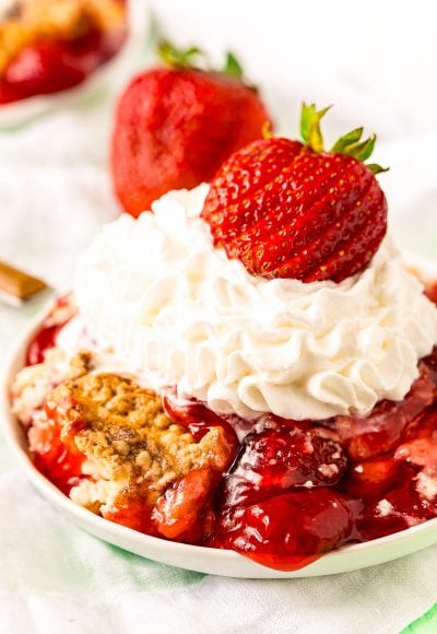 Strawberry dump cake on a white plate topped with whipped cream and a fresh strawberry.