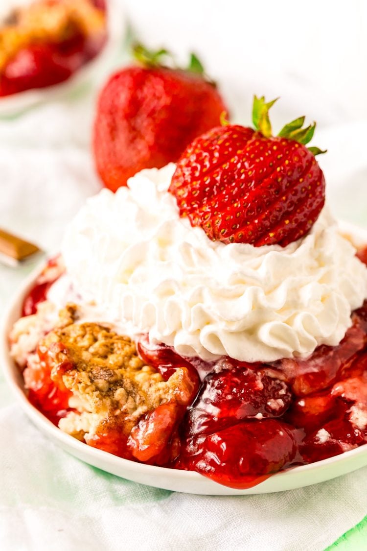 Strawberry dump cake on a white plate topped with whipped cream and a fresh strawberry.