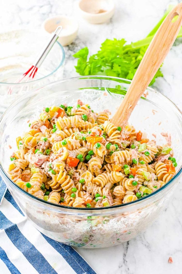 Tuna pasta salad in a glass mixing bowl with a wooden spoon.