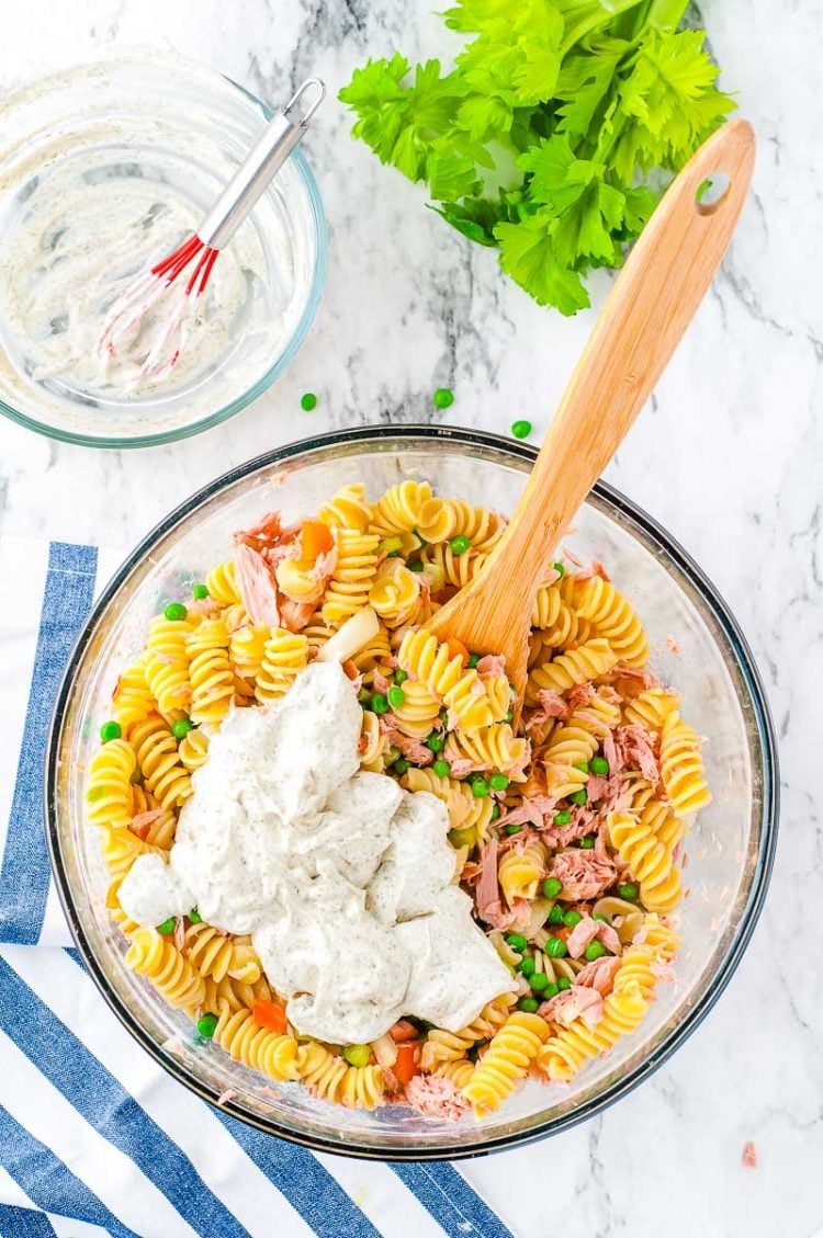 Overhead photo of a glass mixing bowl filled with pasta salad ingredients with a wooden spoon in it.