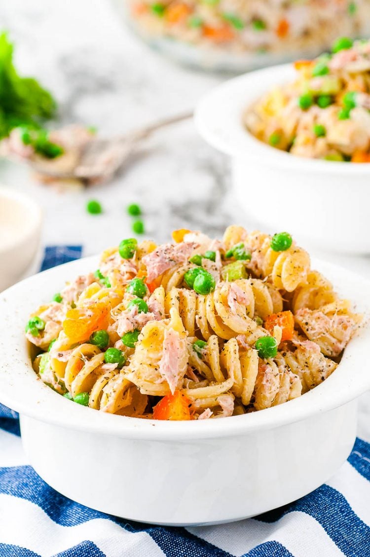 Tuna pasta salad in a white bowl on a white and blue striped napkin.