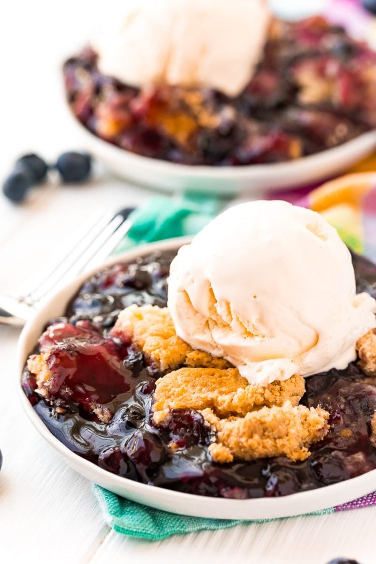 Blueberry dump cake on a white plate topped with a scoop of vanilla ice cream.