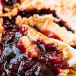 blueberry cobbler in a baking dish with a spoon scooping some out.