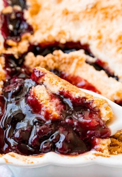 blueberry cobbler in a baking dish with a spoon scooping some out.