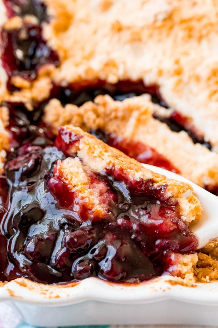 blueberry cobbler in a baking dish with a spoon scooping some out.