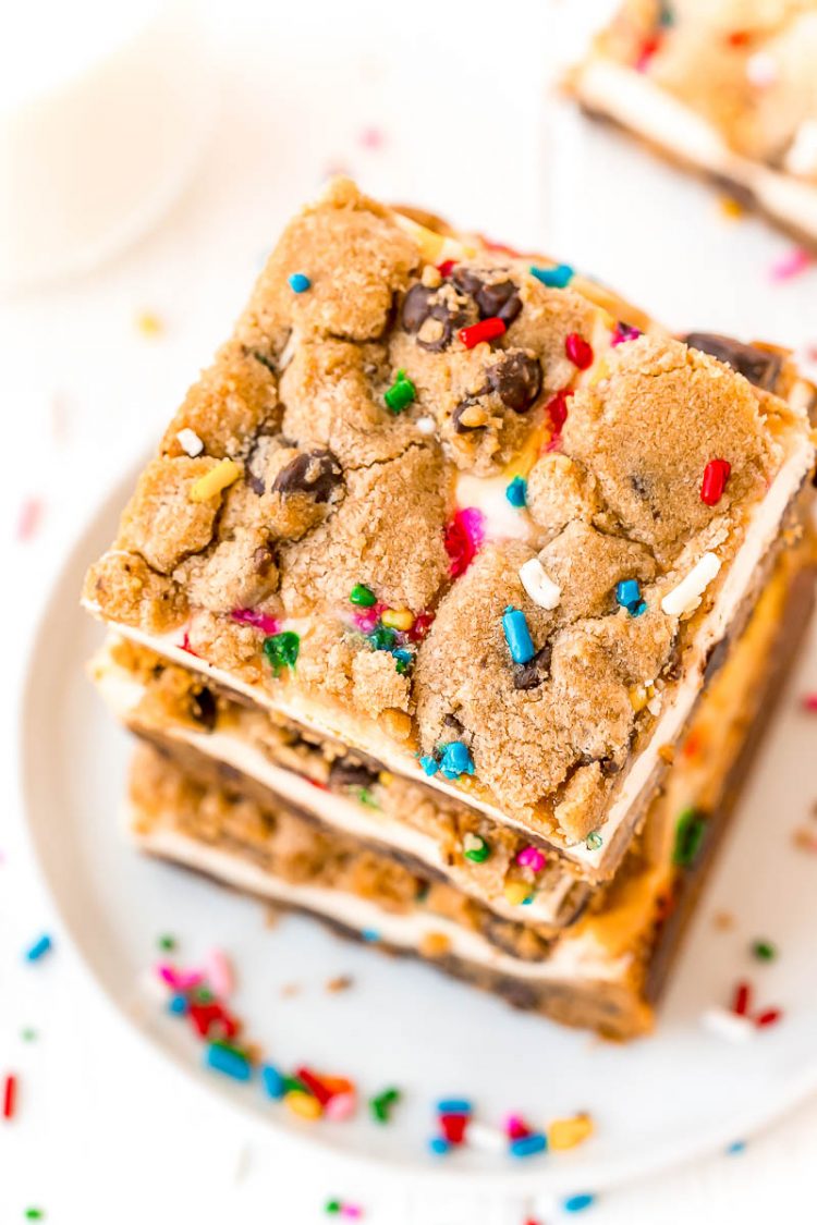 Overhead photo of a stack of chocolate chip cheesecake squares on a white plate with sprinkles scattered around.