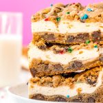 Close up photo of a stack of chocolate chip cookies cheesecake bars on a white plate with sprinkles scattered on the table.