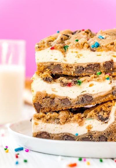 Close up photo of a stack of chocolate chip cookies cheesecake bars on a white plate with sprinkles scattered on the table.