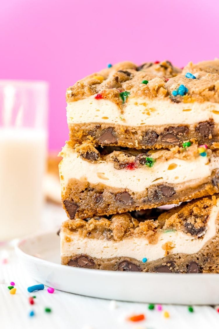Close up photo of a stack of chocolate chip cookies cheesecake bars on a white plate with sprinkles scattered on the table.