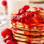 Close up photo of a stack of strawberry pancake covered in strawberry sauce.