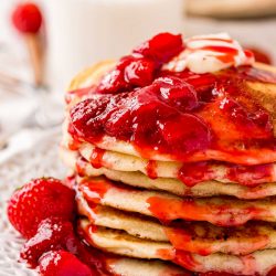Close up photo of a stack of strawberry pancake covered in strawberry sauce.