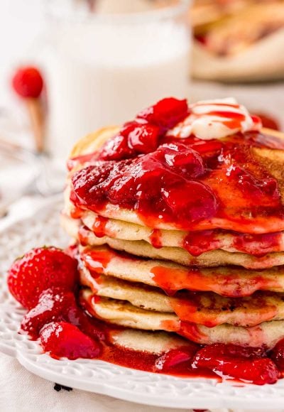 Close up photo of a stack of strawberry pancake covered in strawberry sauce.