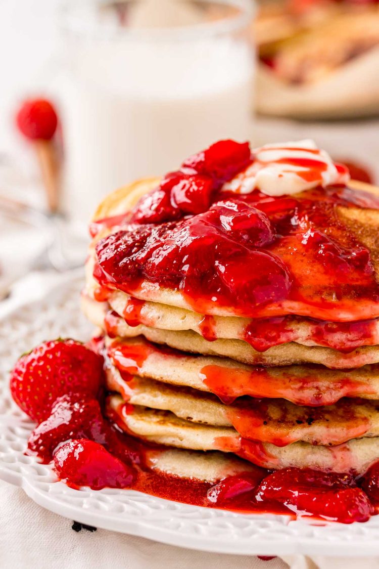 Close up photo of a stack of strawberry pancake covered in strawberry sauce.