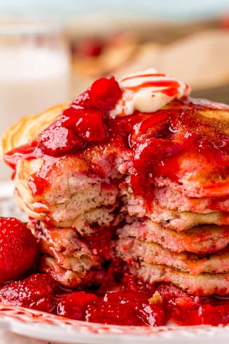 A stack of strawberry pancakes covered in strawberry sauce with a bite taken out of it.