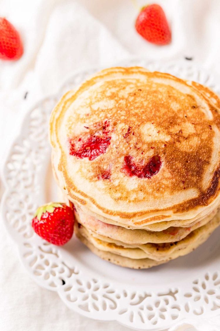 A stack of strawberry pancakes on a white plate.