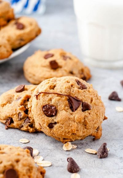 Chocolate Chip cookies on a counter with chocolate chips scattered around and a glass of milk in the background.