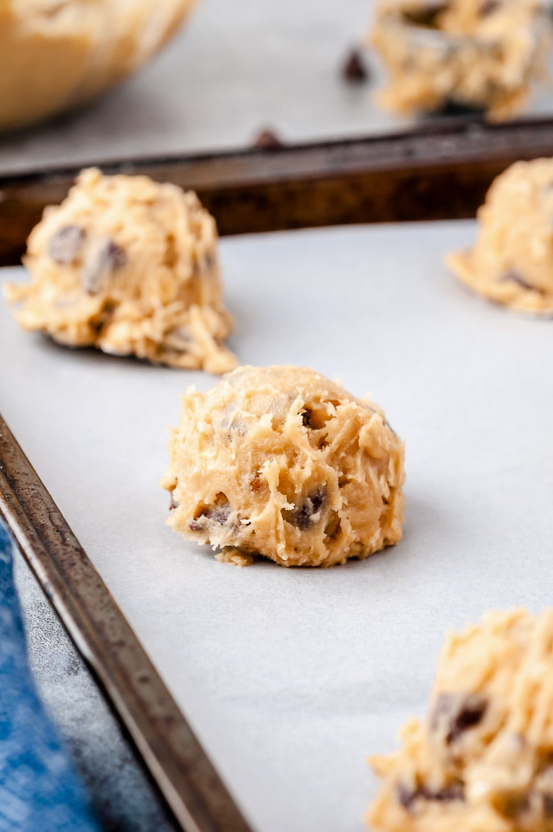 Scoop of cookie dough on a parchment lined baking sheet.