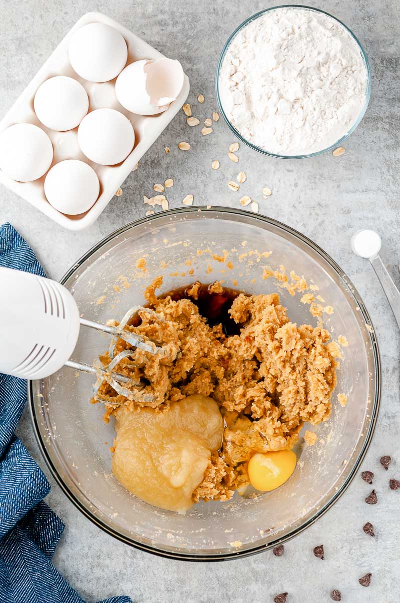 Ingredients being blended to make oatmeal chocolate chip cookies in a large glass bowl.