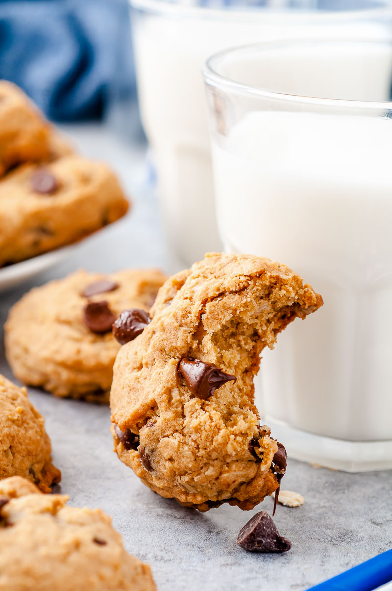 Oatmeal chocolate chip cookie with a bite taken out of it leaning against a glass of milk.