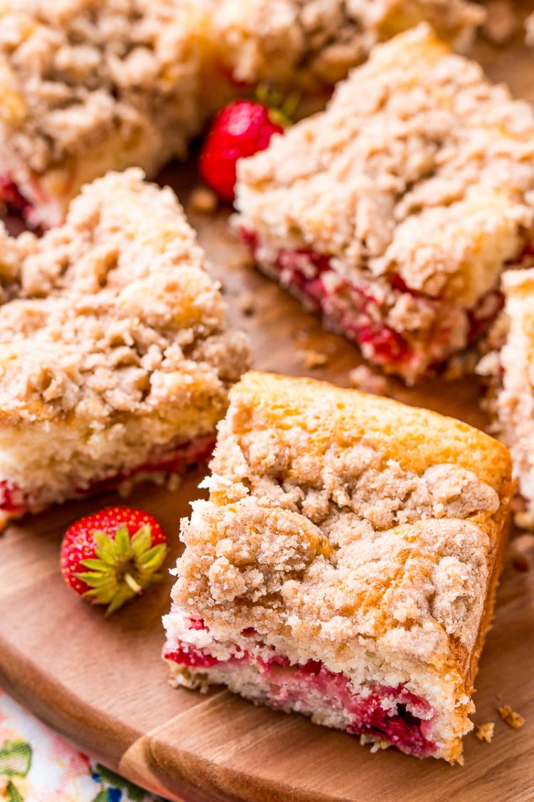 Slices of coffee cake on a wooden cutting board with strawberries scattered around.