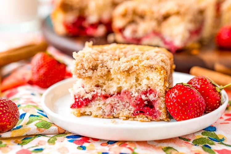 Strawberry coffee cake slice sitting on a white dessert plate with more strawberries scattered around.