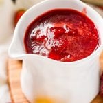Strawberry sauce in a white serving cup with strawberries and lemons scattered around it.
