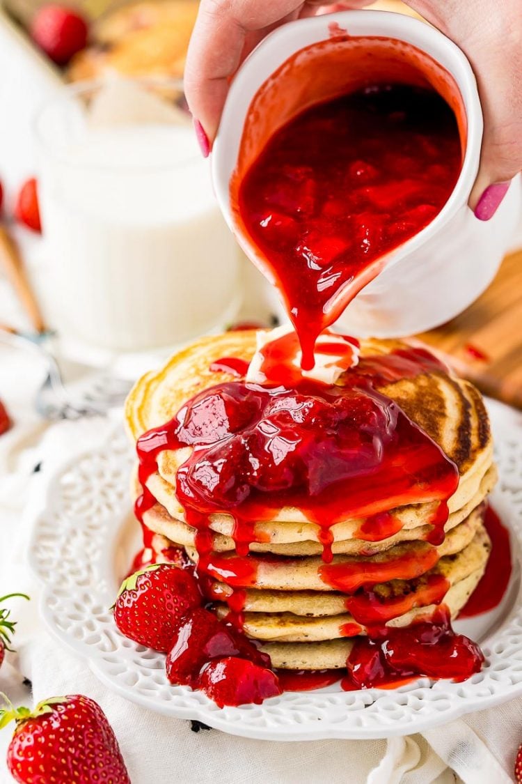 A stack of pancakes with strawberry sauce being poured over it.