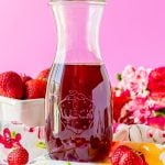 Glass carafe filled with strawberry simple syrup.