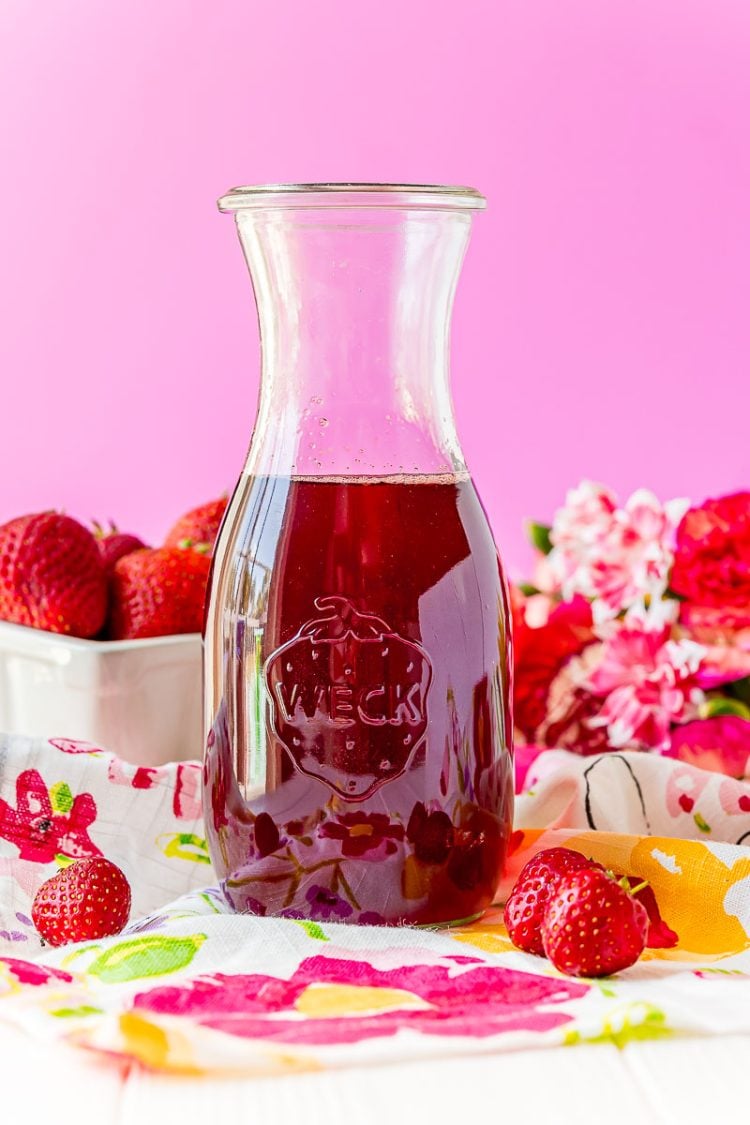 Glass carafe filled with strawberry simple syrup.