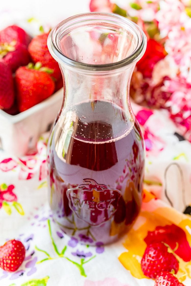 A glass carafe filled with strawberry simple syrup on a colorful napkin.