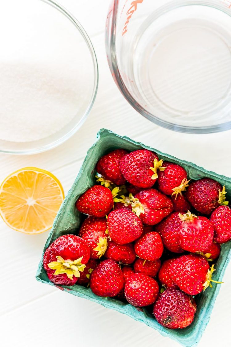 Ingredients to make strawberry simple syrup on a white table.