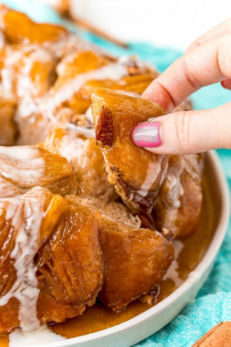 A woman's fingers pulling a piece of monkey bread away from the rest of the bread. 