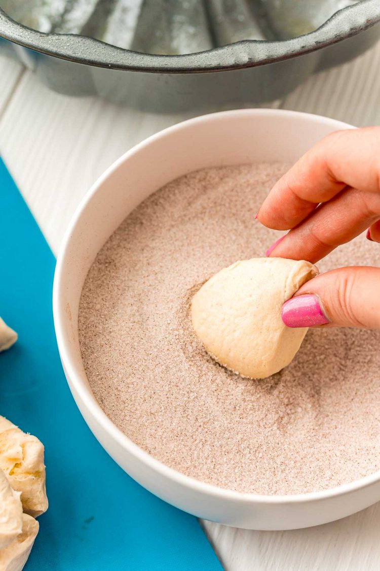 Pieces of biscuit being rolled in cinnamon sugar.